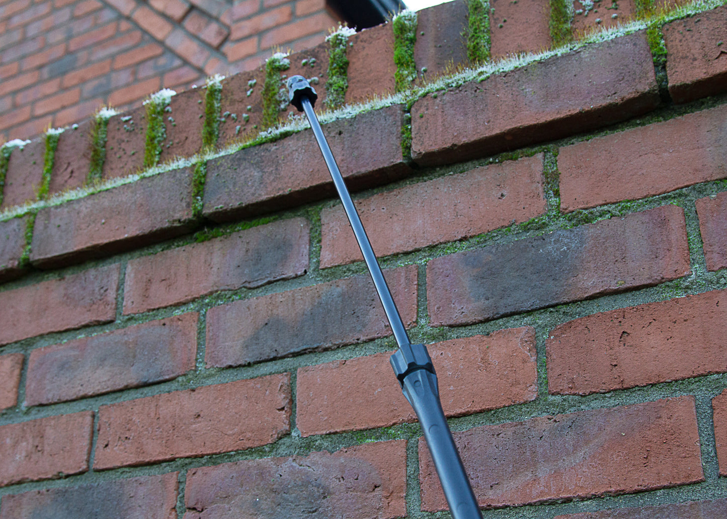 photo showing the telescopic lance, for our garden sprayers, fully extended and being used to spray moss killer on to a brick wall